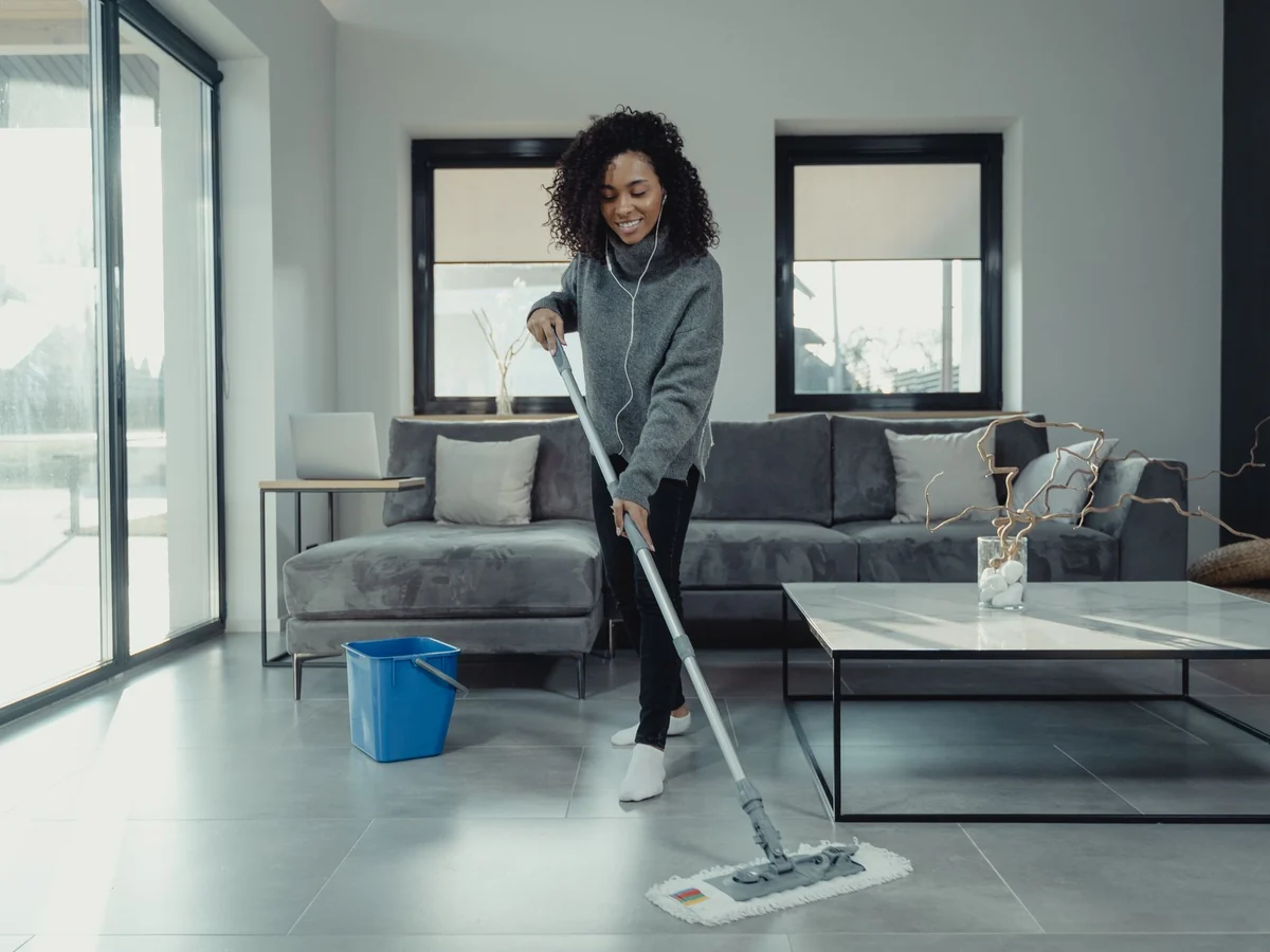 Example photo: a cleaner mopping the floor of a bright living room during recurring house cleaning